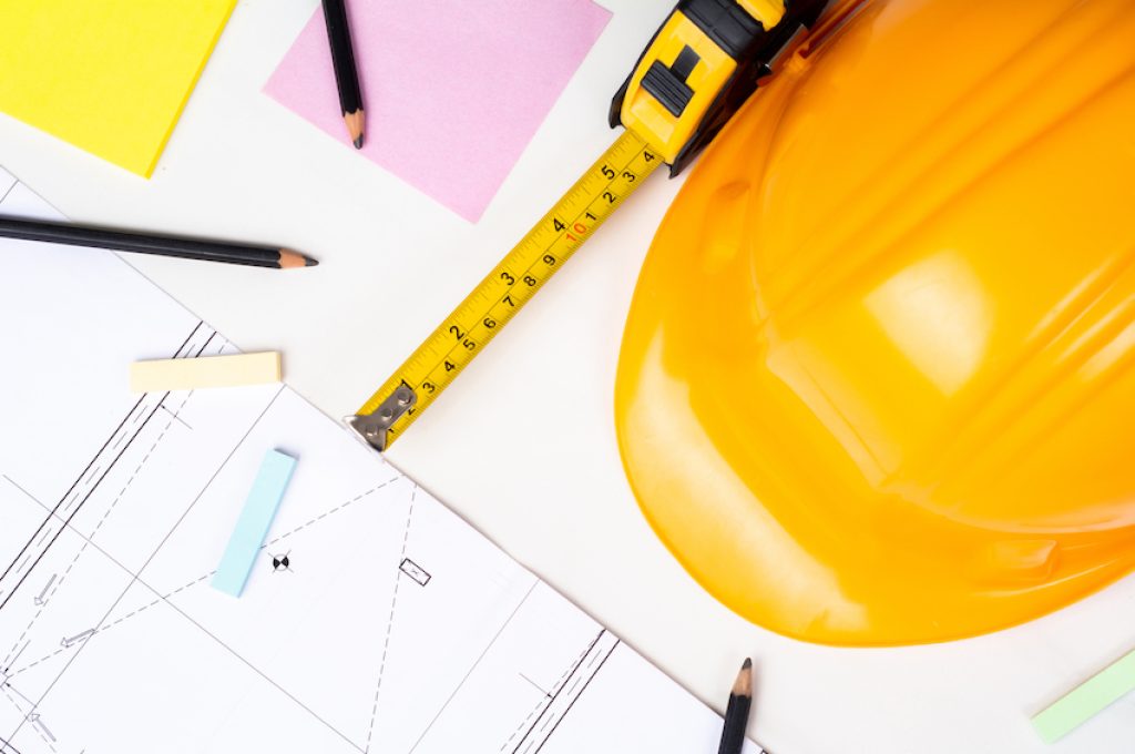 Close-up of blueprints, measuring tape and yellow construction helmet. Engineer concept