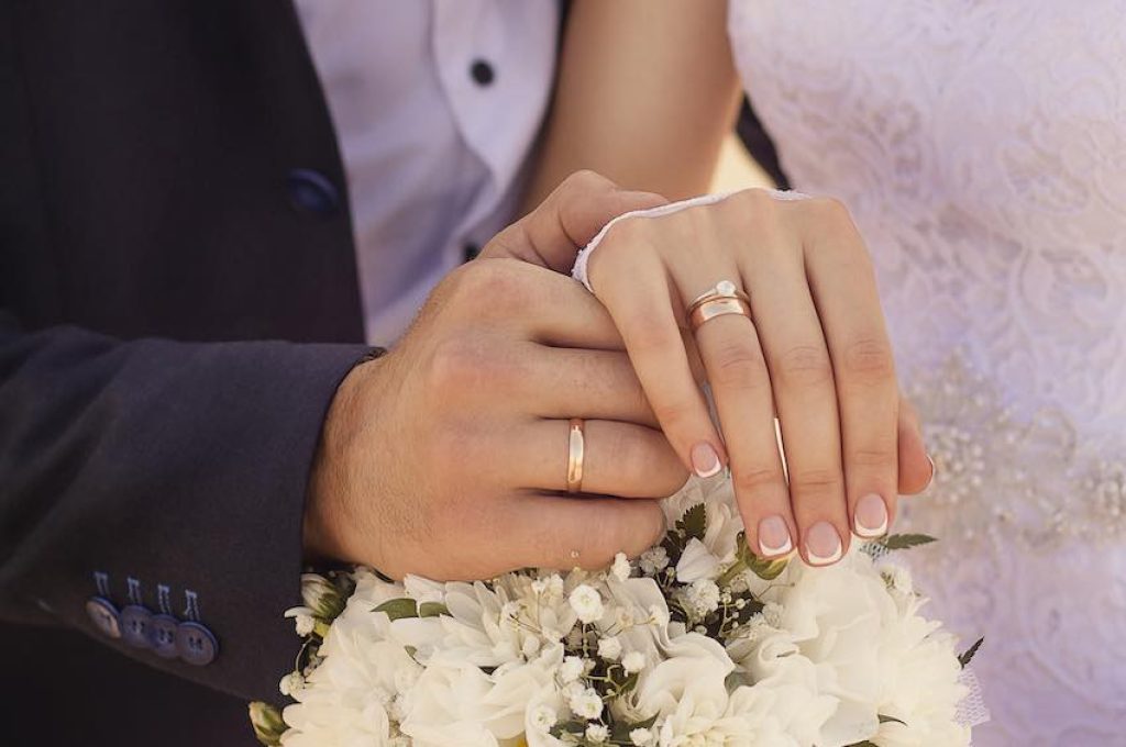 A closeup shot of newlyweds holding hands and showing the wedding rings