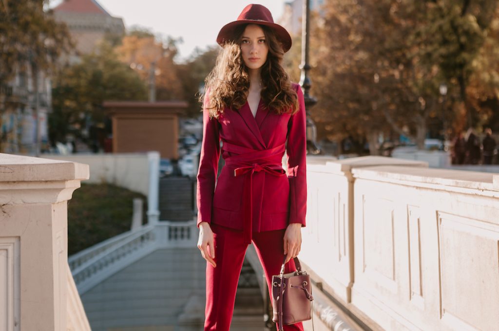 beautiful stylish woman in purple suit walking in city street, spring summer autumn season fashion trend wearing hat, holding purse